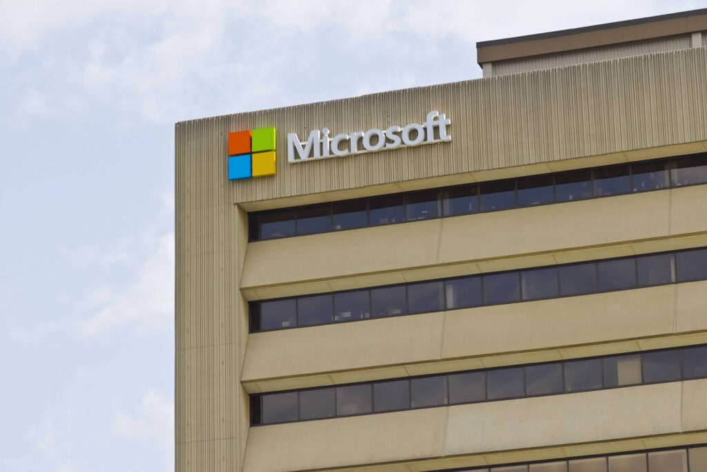 Vista exterior de un edificio de oficinas de Microsoft con el logotipo de la compañía en la parte superior de la fachada, bajo un cielo parcialmente nublado.