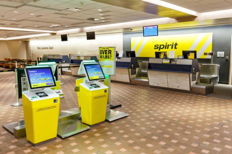 Mostrador de atención y kioscos amarillos de auto check-in de Spirit Airlines en el área de documentación de un aeropuerto, con señalización para equipaje y pantallas de servicio.