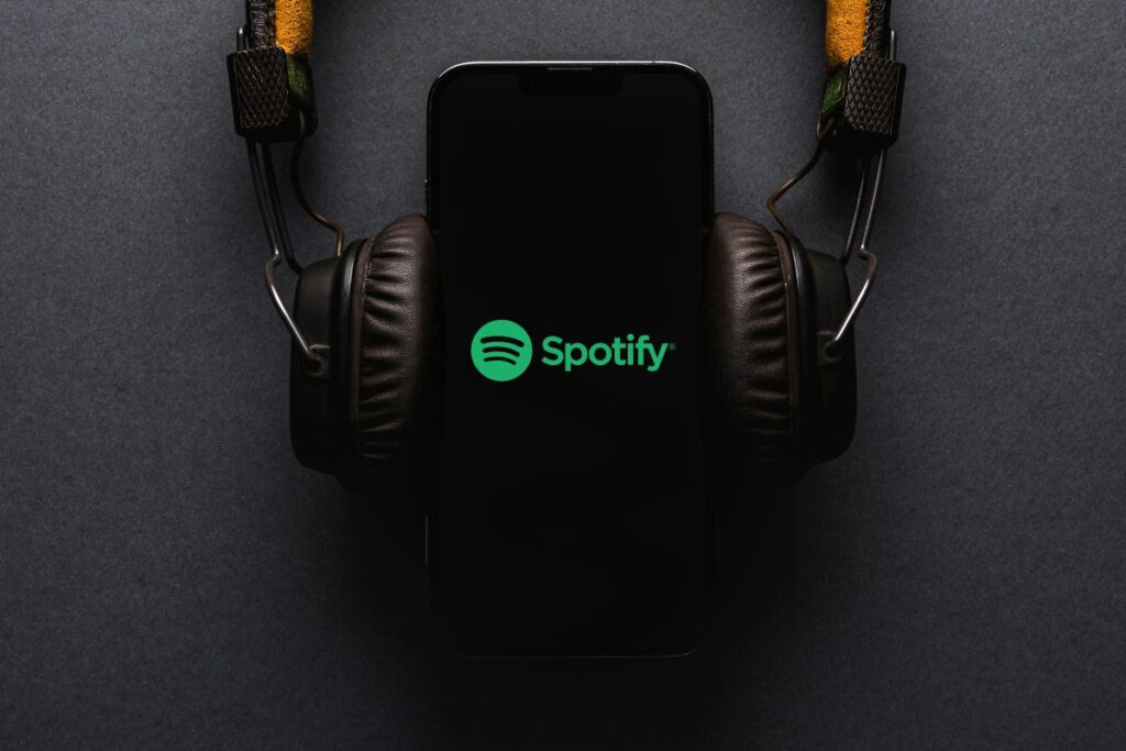 Teléfono con logo de Spotify y audífonos, ilustrando el aumento de precios y nuevas funciones premium para impulsar crecimiento