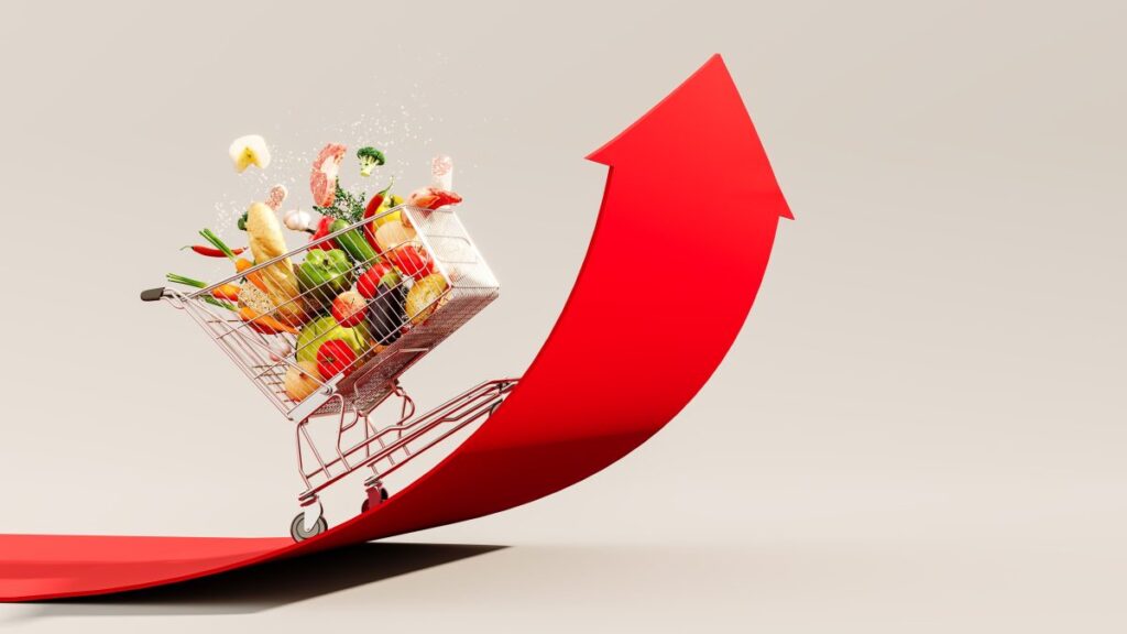 Carrito de supermercado lleno de alimentos subiendo por una flecha roja que simboliza el aumento de precios en Estados Unidos
