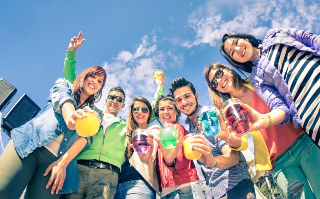 Grupo de jóvenes de la Generación Z brindando con bebidas coloridas bajo el sol, símbolo de nuevos hábitos de consumo y bienestar.