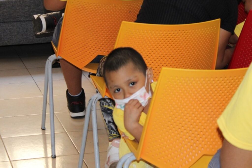 Niño con camiseta amarilla y cubrebocas sentado entre sillas naranjas durante una jornada organizada por AMANC Veracruz y Grupo Duxon. La imagen refleja el espíritu de esperanza y apoyo a la niñez impulsado por Omar Anitua Valdovinos a través de esta alianza solidaria.