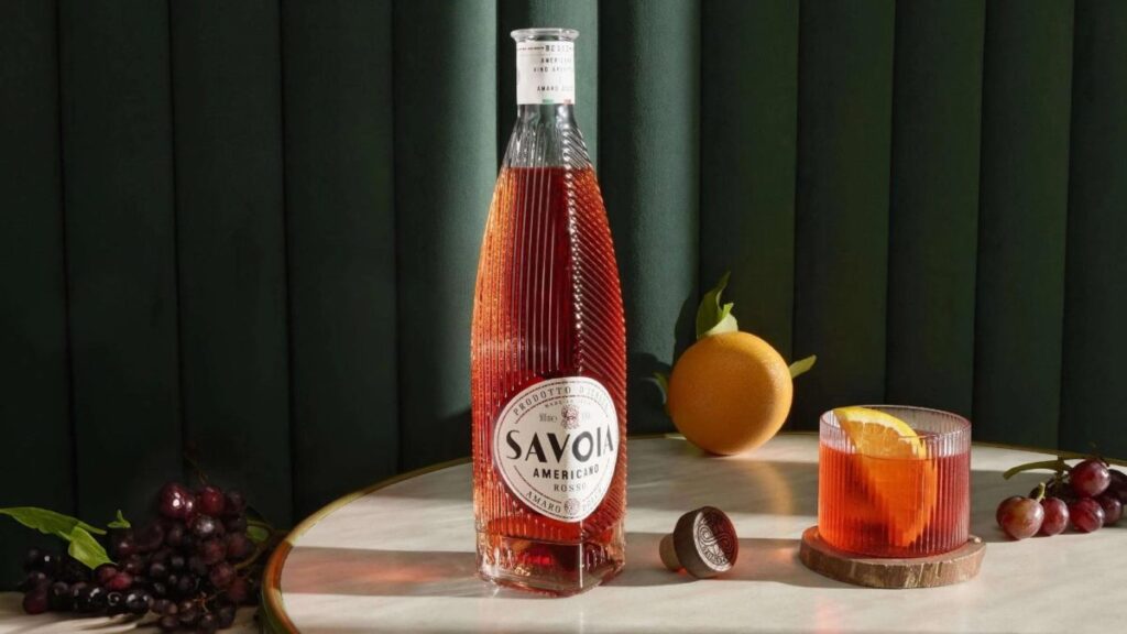 Botella de Savoia Americano Rosso sobre mesa elegante con copa de aperitivo y frutas frescas, en estilo fotográfico aspiracional y profesional.