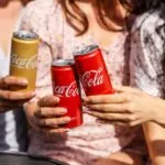 Personas celebrando con latas de Coca-Cola, símbolo de diversidad y empleo inclusivo