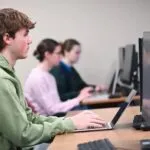 Estudiantes universitarios trabajando con computadoras y herramientas de inteligencia artificial en campus moderno
