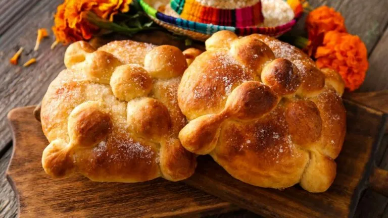 Pan de muerto tradicional mexicano cubierto de azúcar y decorado con figuras de huesos, acompañado de flores de cempasúchil.